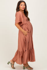woman wearing a rust-colored maternity maxi dress with short sleeves and a tiered ruffle hem, showcasing her baby bump