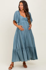 woman wearing a teal maternity maxi dress with flutter sleeves and a tiered hem, gently cradling her baby bump