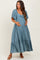 woman wearing a teal maternity maxi dress with flutter sleeves and a tiered hem, gently cradling her baby bump
