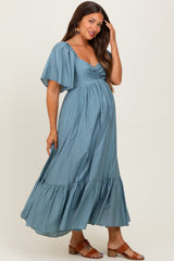 woman wearing a dusty blue maternity maxi dress with flutter sleeves and a tiered hem, showing her baby bump