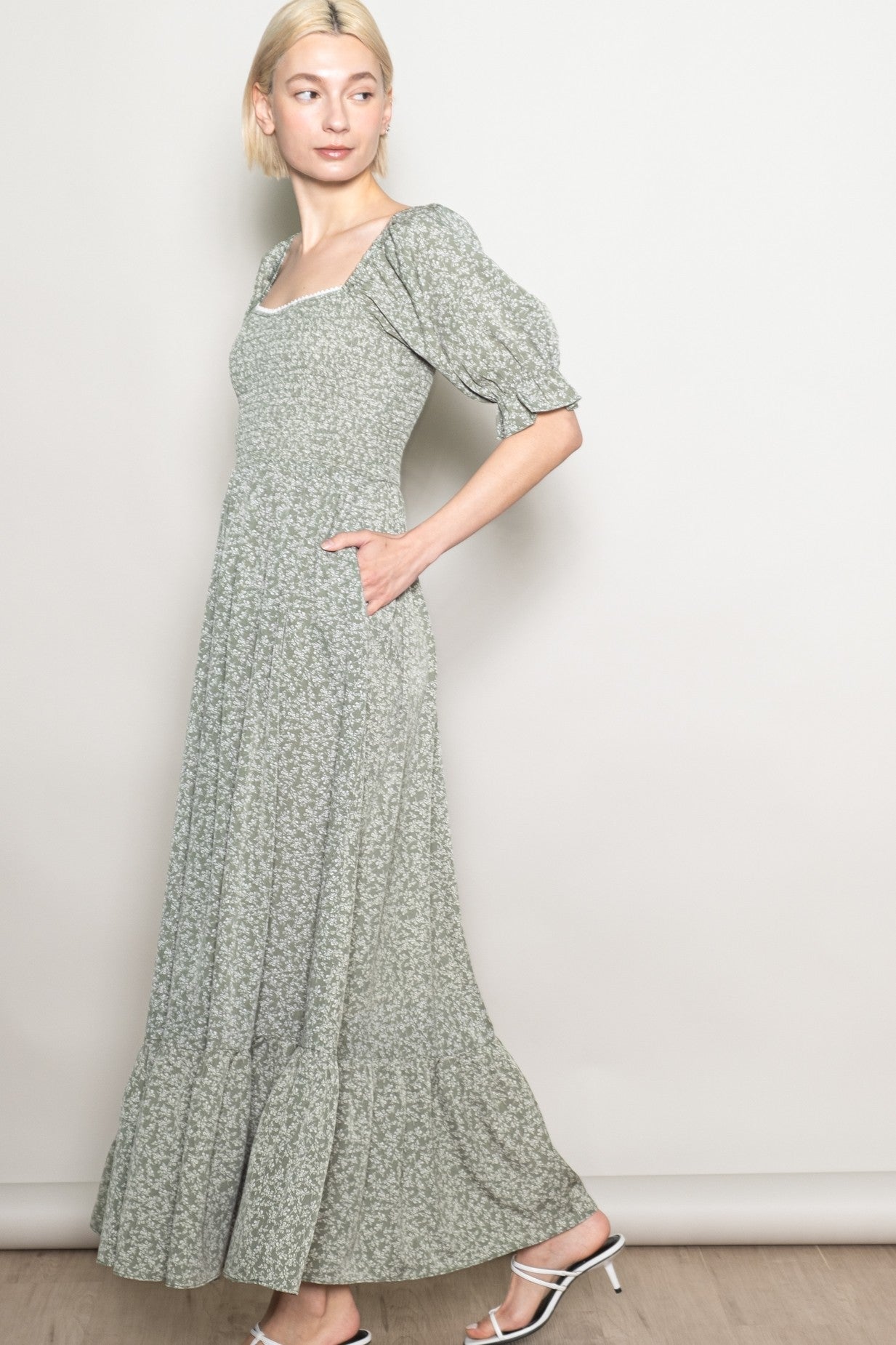 woman wearing a light green floral maxi dress with puff sleeves and side pockets, standing sideways against a neutral background