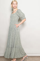 woman wearing a light green floral maxi dress with puff sleeves and side pockets, standing sideways against a neutral background