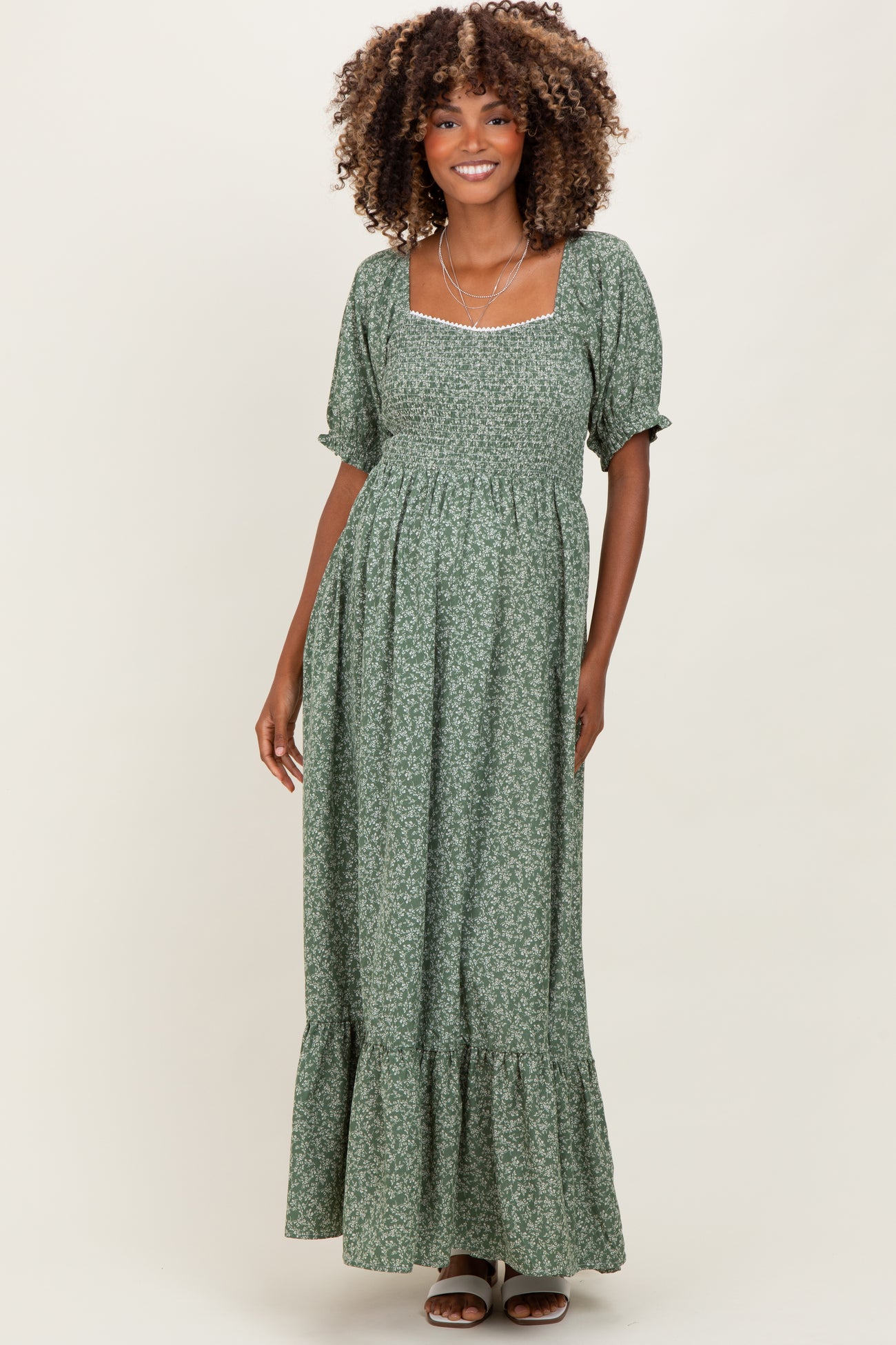 woman wearing a green floral maternity dress with puff sleeves and a ruffled hem, smiling at the camera