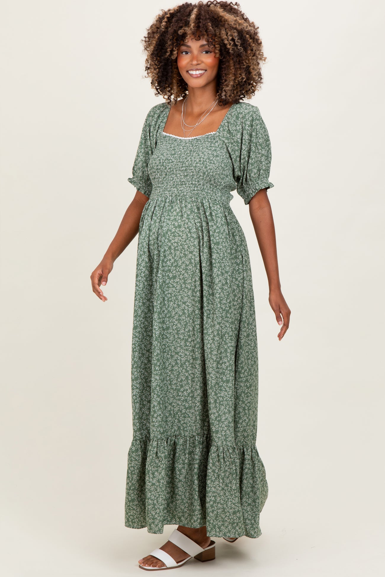 woman wearing a green floral maternity maxi dress with puff sleeves and a ruffled hem, showcasing her baby bump