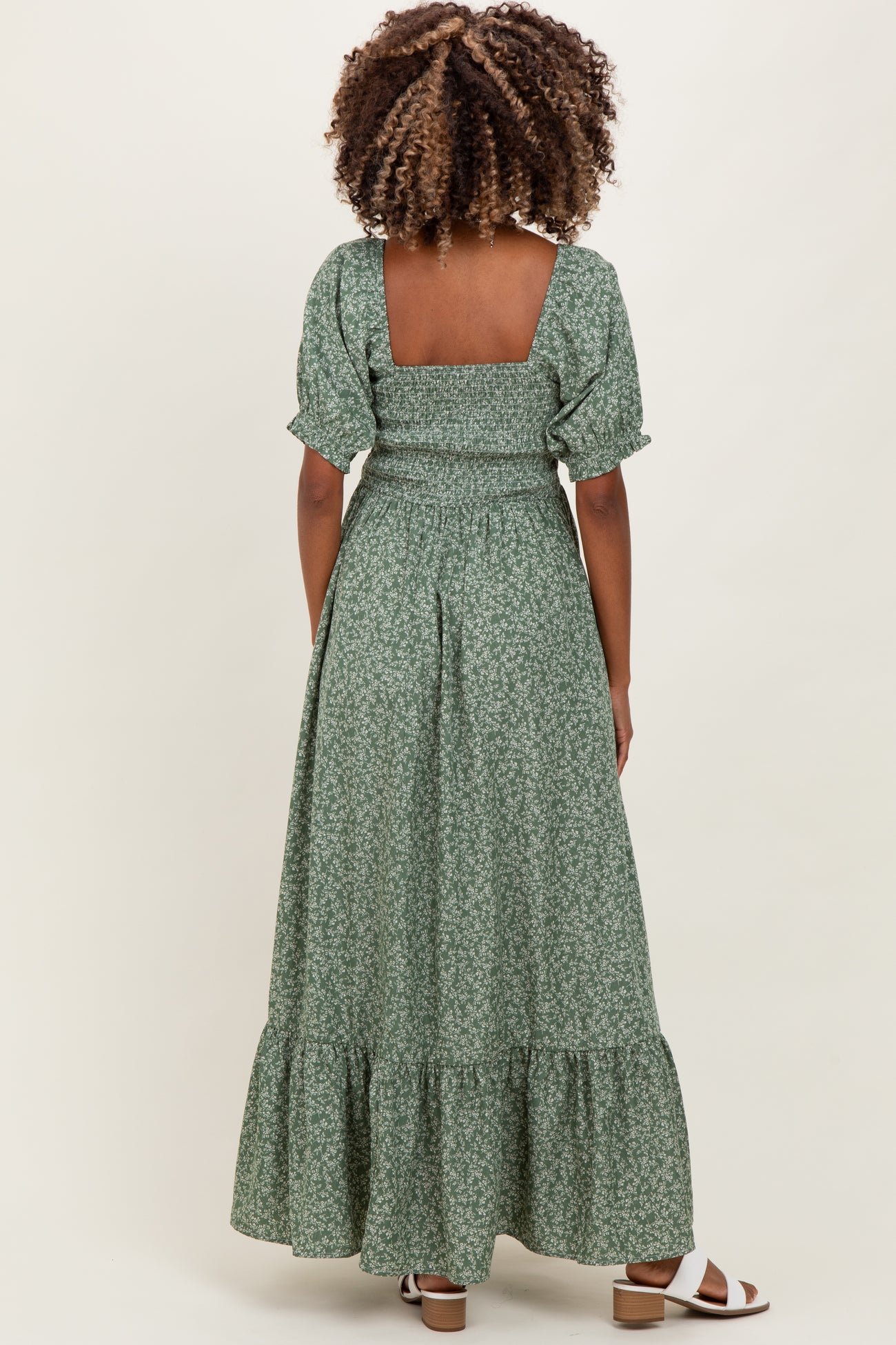 woman wearing a green floral print maternity maxi dress with puff sleeves and a tiered skirt, showing a baby bump