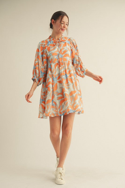 woman wearing an orange and blue floral print short sleeve dress with a tie neck and balloon sleeves