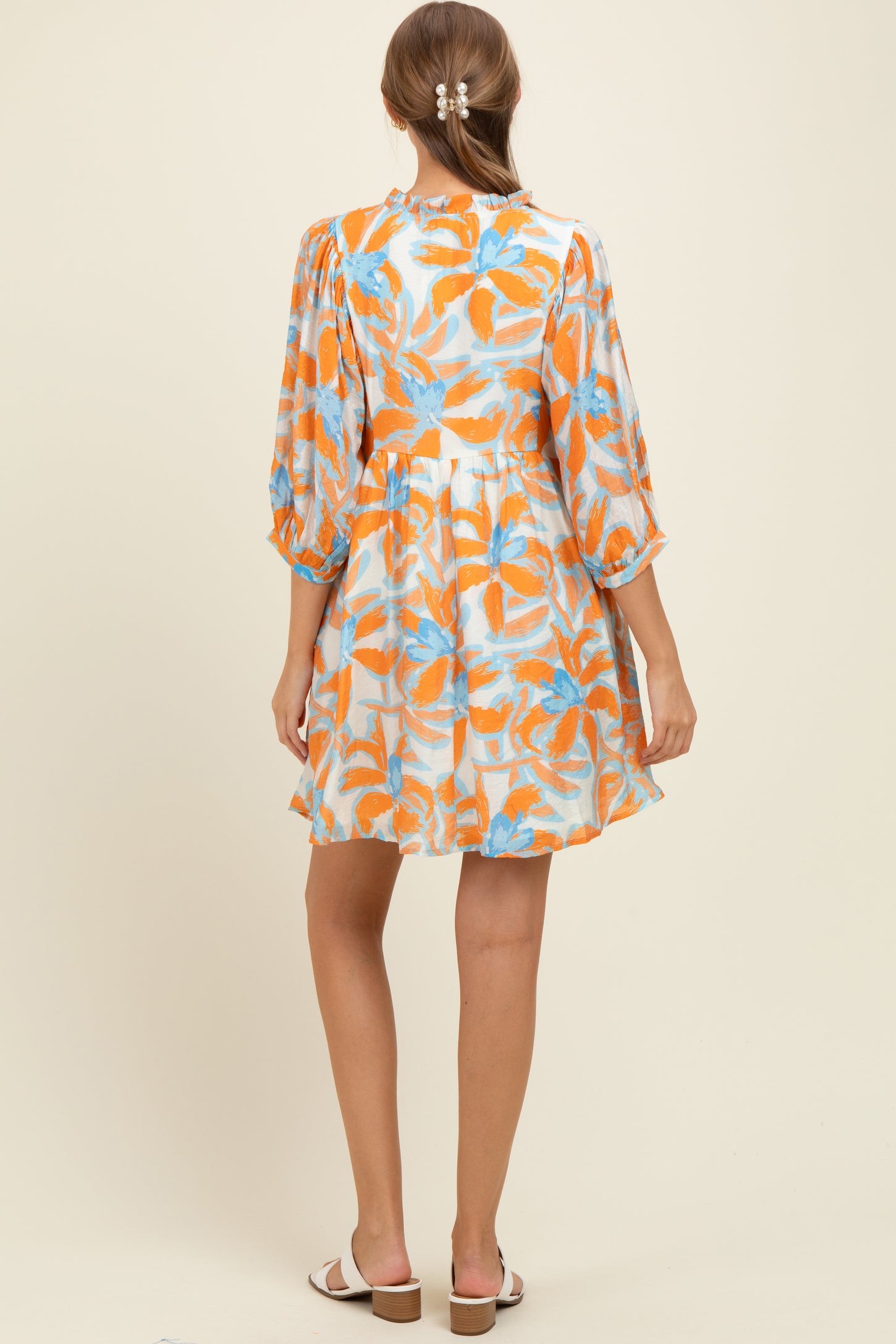woman wearing a floral print maternity dress with orange and blue hues, showing a relaxed fit and balloon sleeves