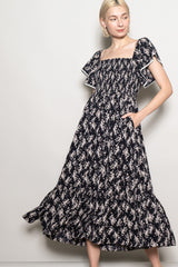 woman wearing a black floral print maxi dress with short ruffled sleeves and side pockets