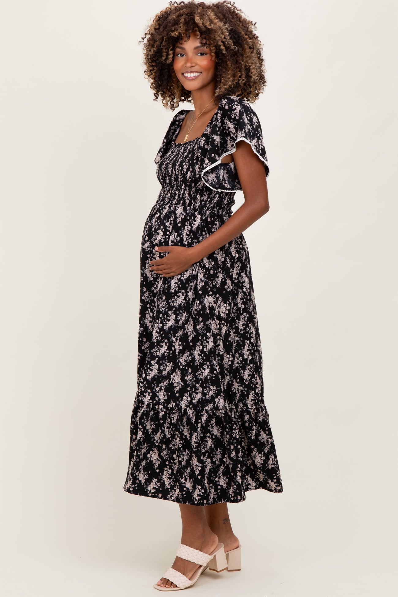 woman wearing a black floral maternity maxi dress and holding her baby bump