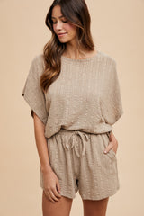 woman wearing a beige textured short-sleeve romper with a cinched waist and side pockets