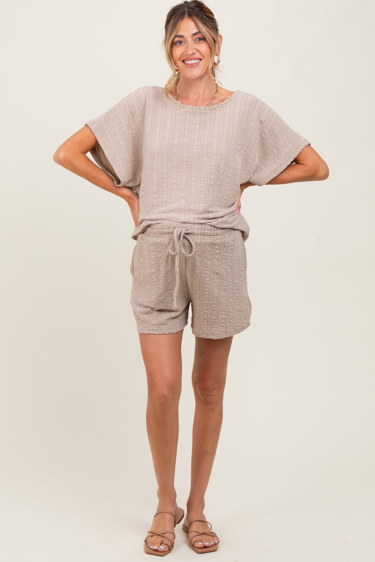 woman wearing a beige short sleeve maternity romper with a drawstring waist and relaxed fit