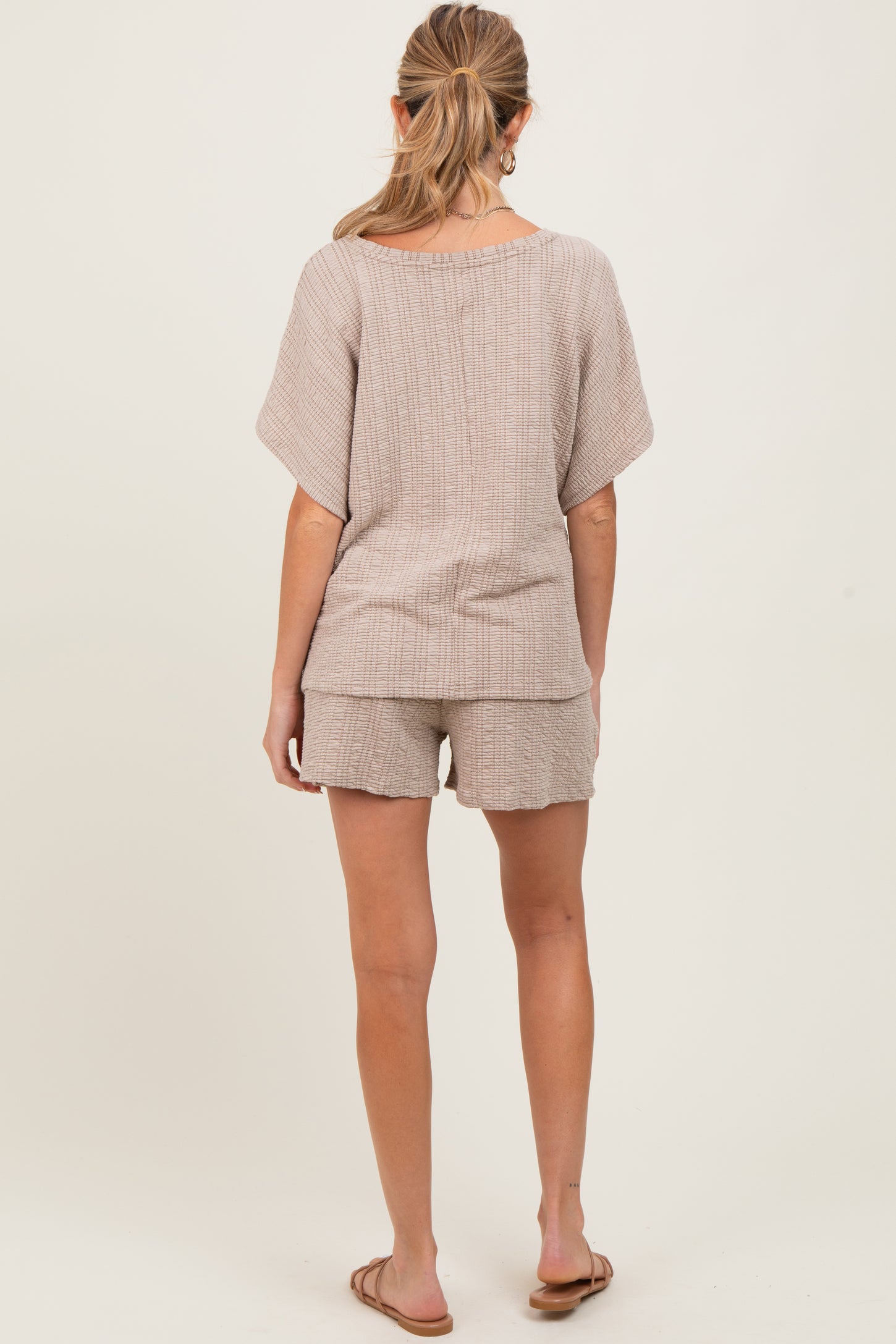 woman wearing a beige maternity knit top and matching shorts, view from the back