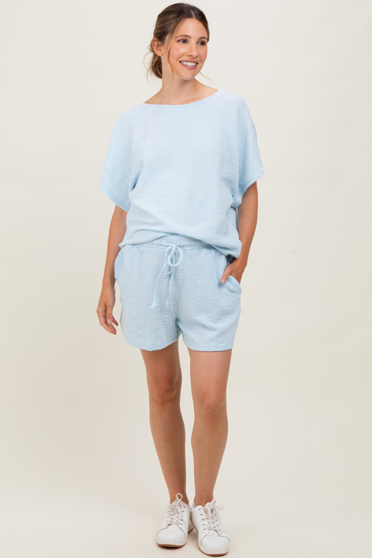 woman wearing a light blue maternity short set with a loose top and shorts, featuring pockets