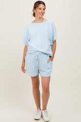 woman wearing a light blue maternity short set with a loose top and shorts, featuring pockets