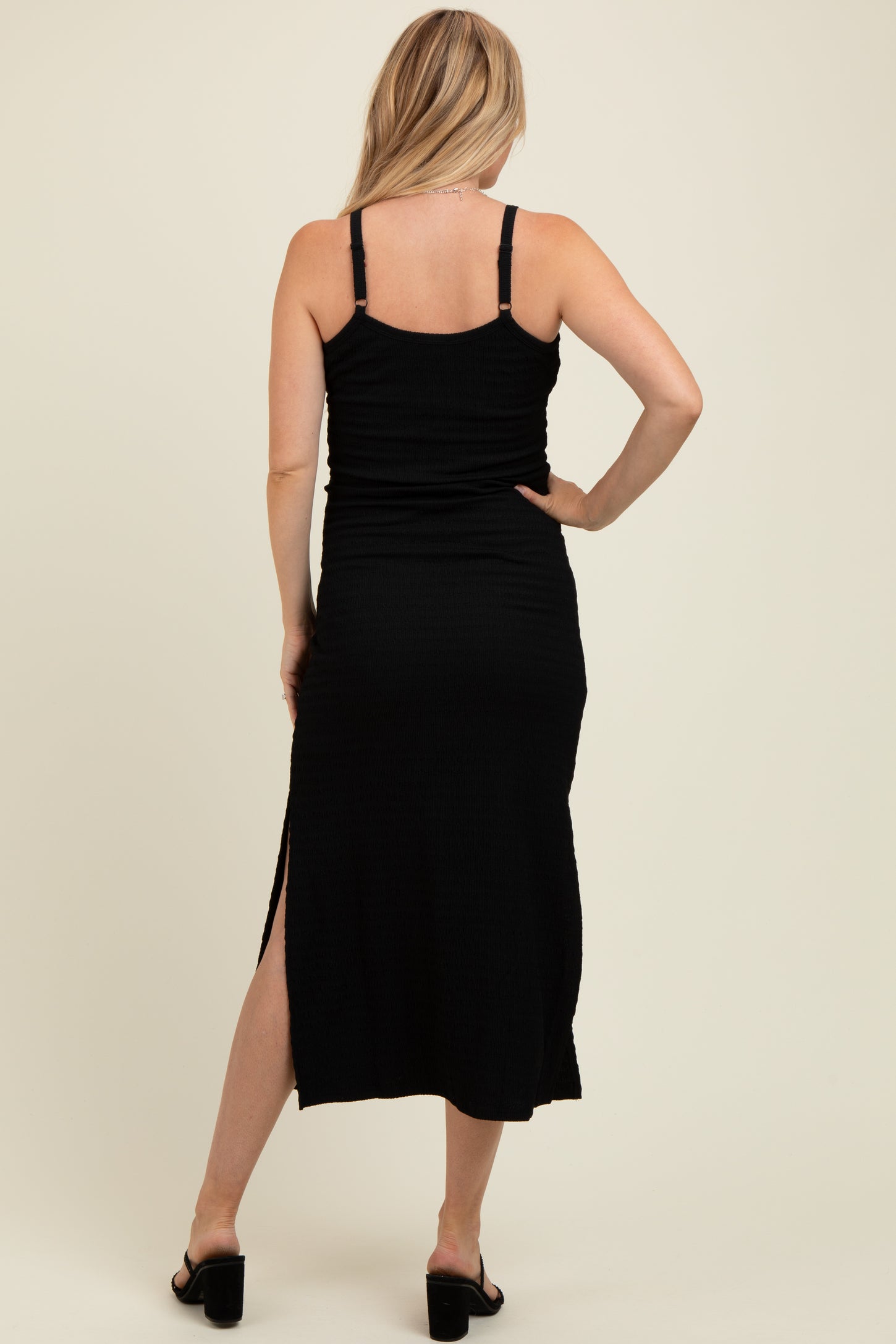 woman wearing a black maternity maxi dress with side slits and adjustable straps, showing her back