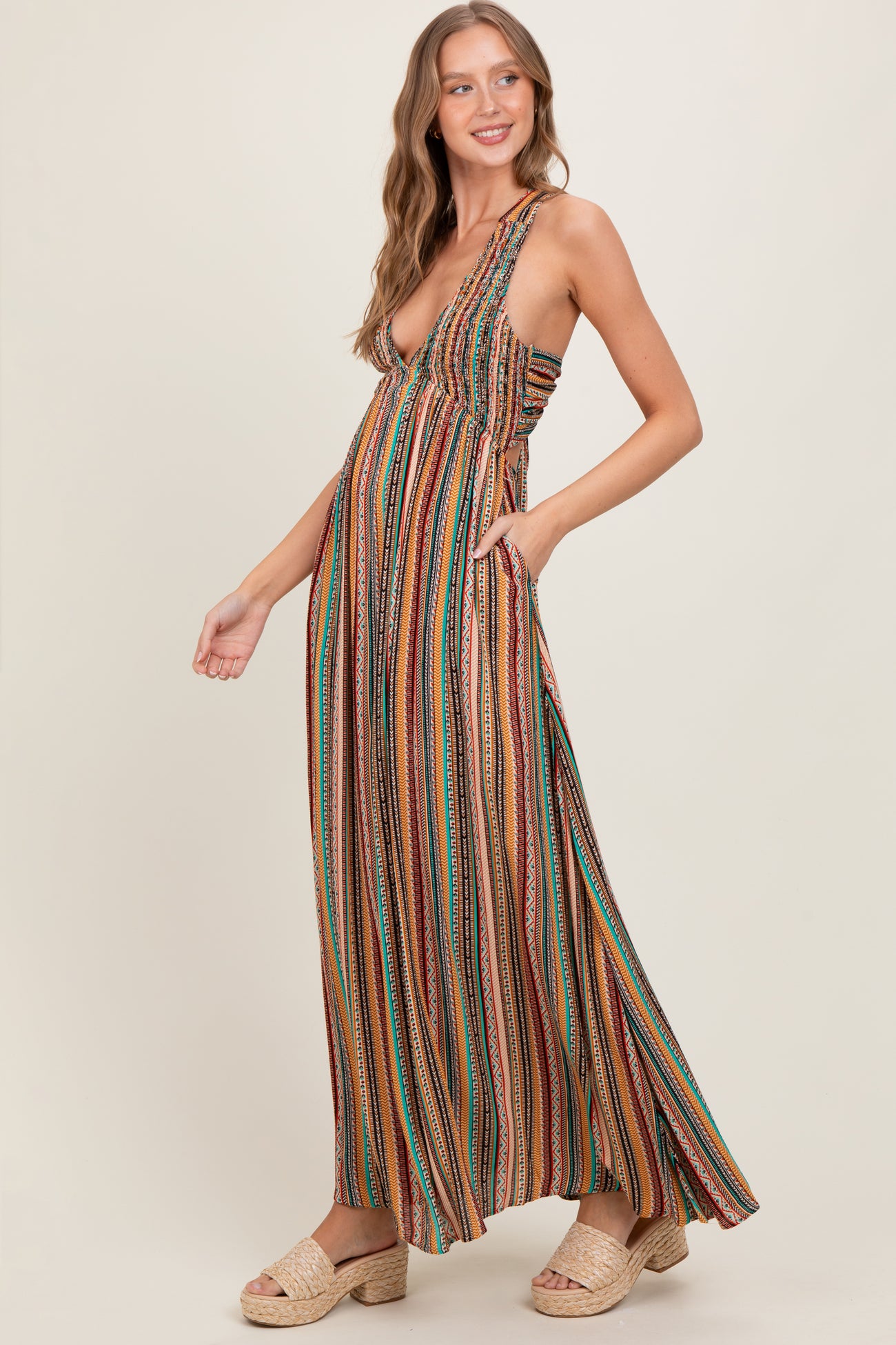 woman wearing a multi-colored striped maxi dress with a deep neckline and pockets, smiling and standing in profile