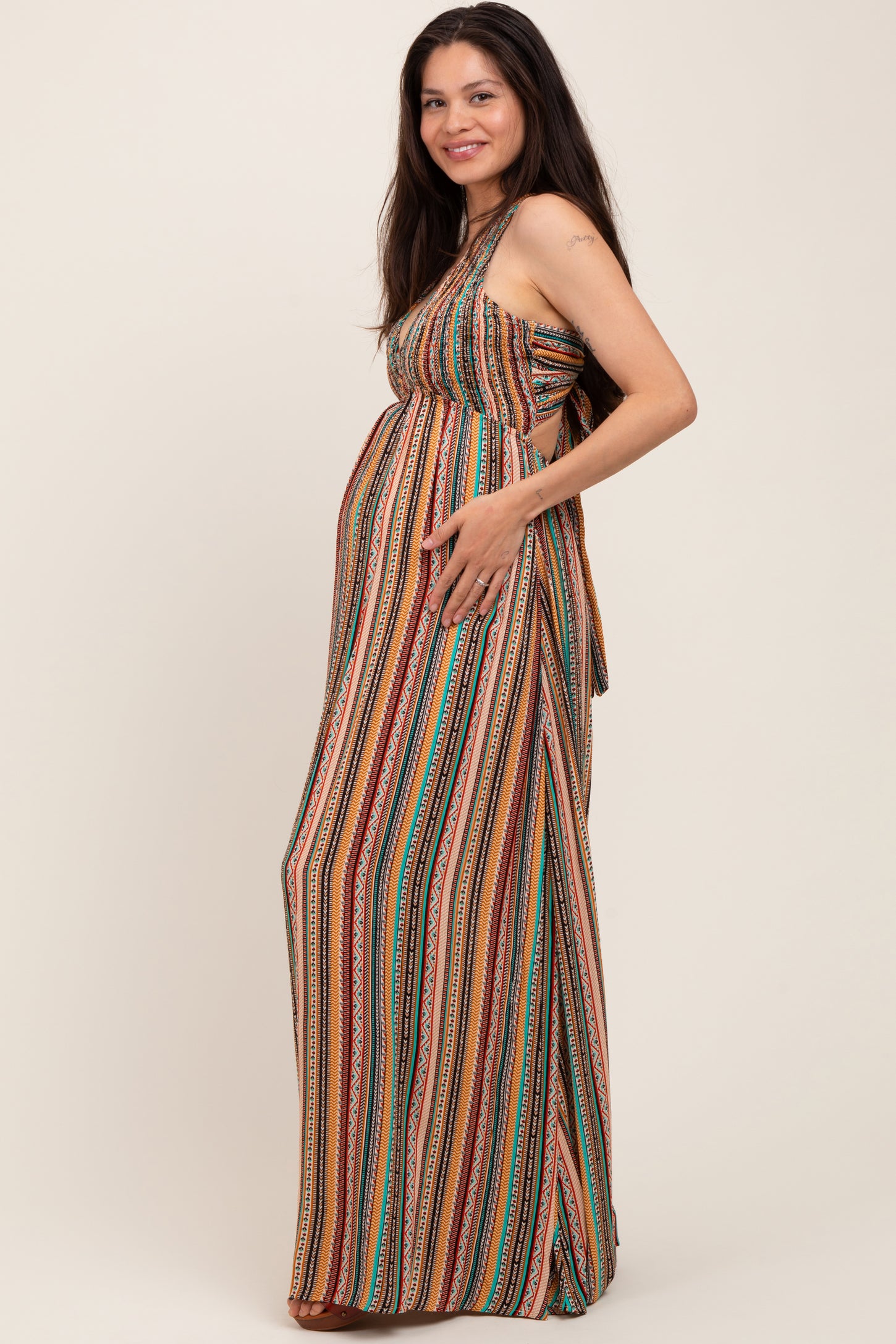 woman wearing a multicolored striped maternity maxi dress and gently holding her baby bump