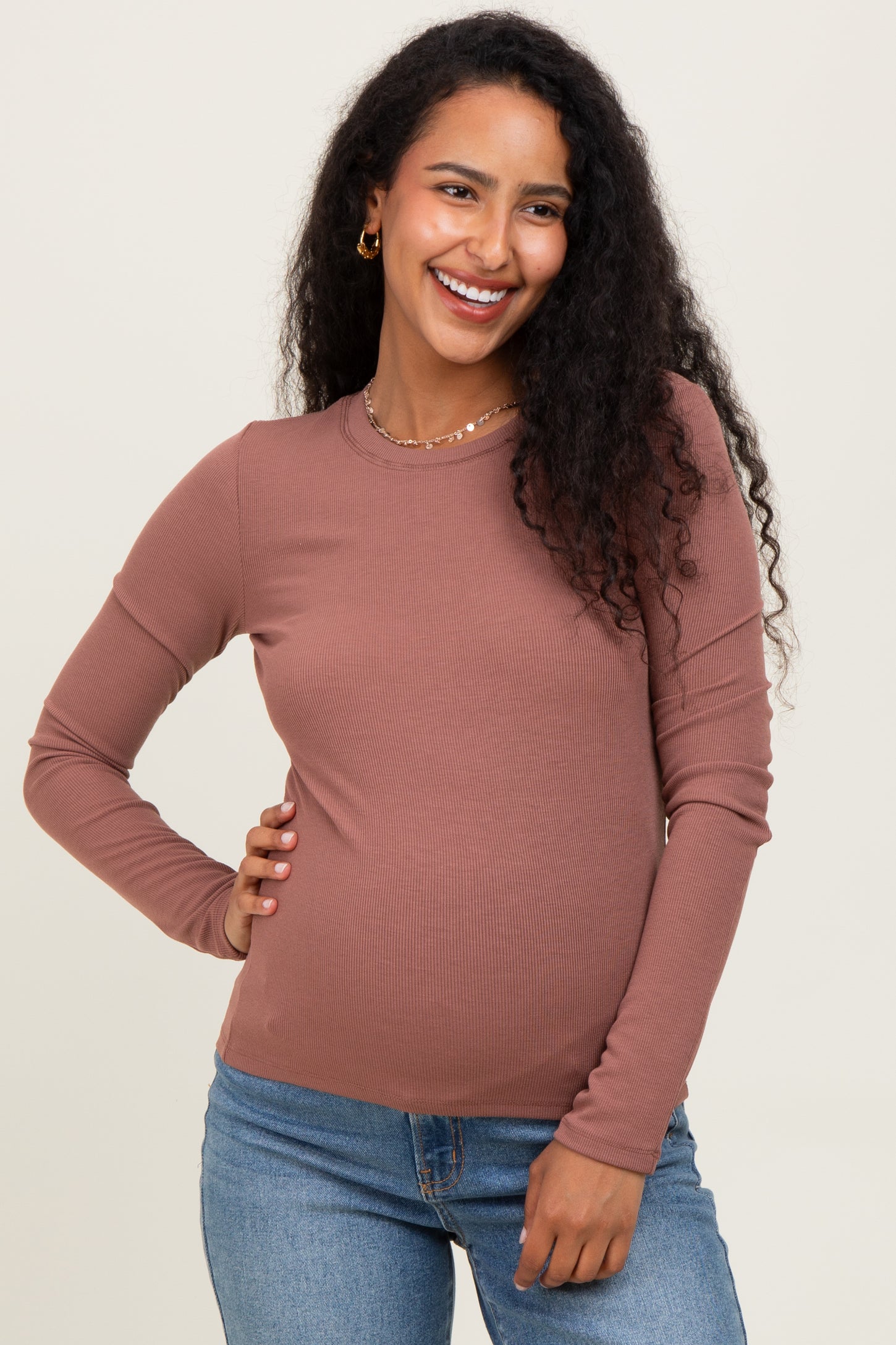 woman wearing a rust colored long sleeve maternity top with a visible baby bump and smiling