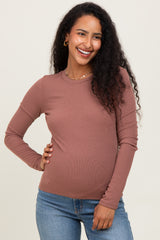 woman wearing a rust colored long sleeve maternity top with a visible baby bump and smiling