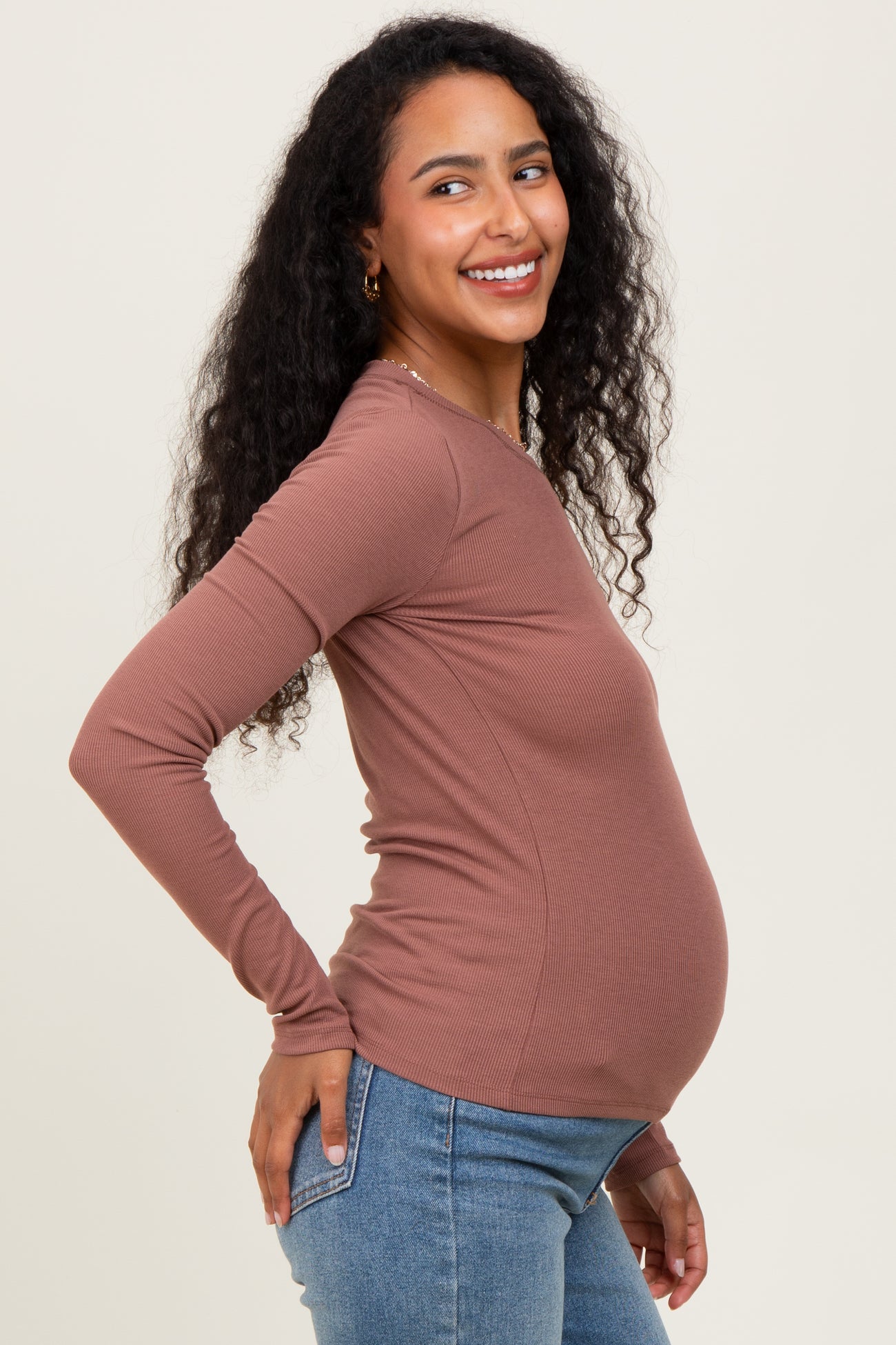 woman wearing a brown long sleeve maternity top and showing her baby bump