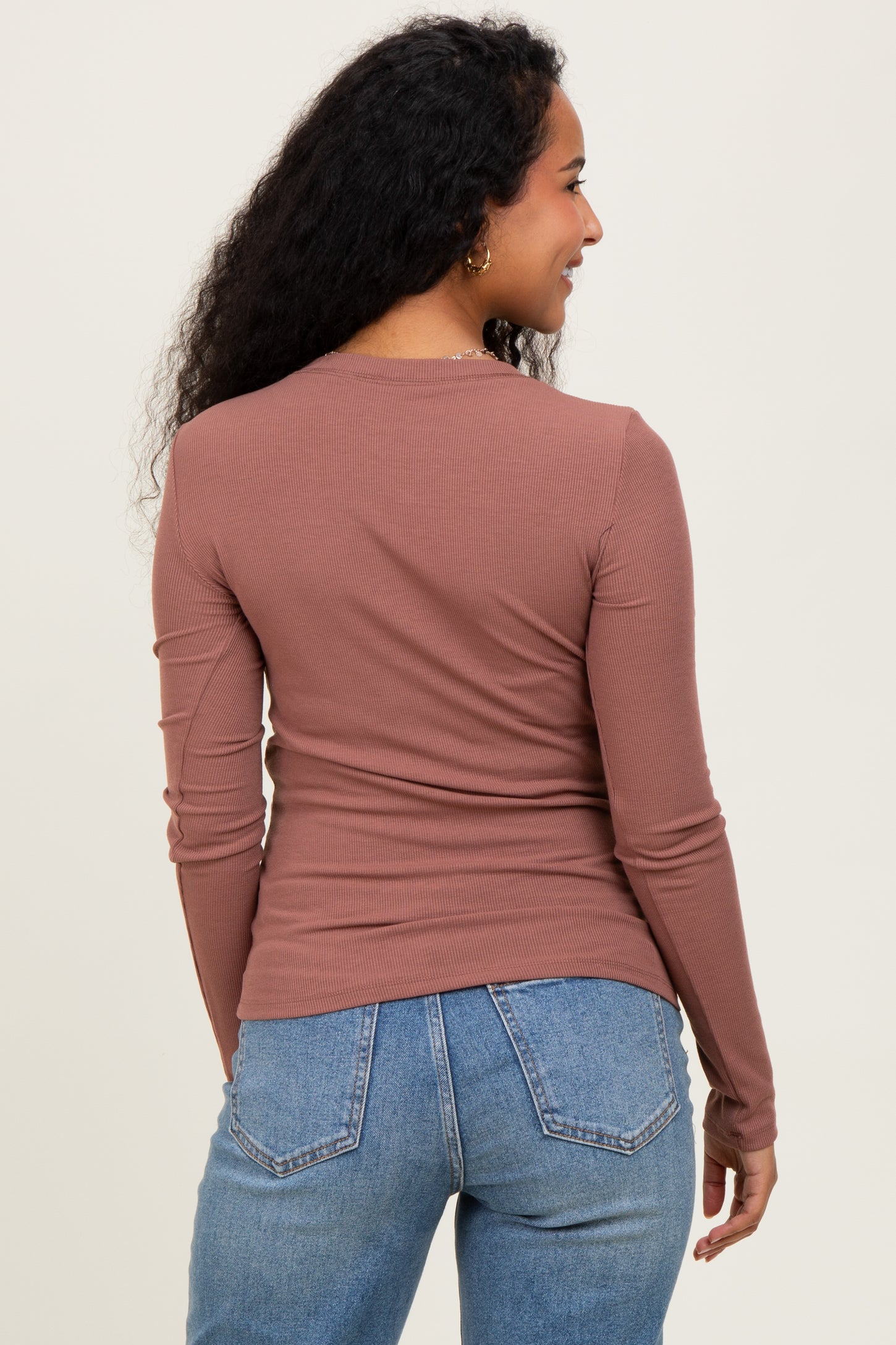 woman wearing a mauve long sleeve maternity top, shown from the back, paired with light blue jeans