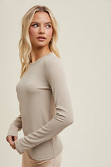 woman wearing a fitted beige long sleeve top with a round neckline, styled with a slight side view