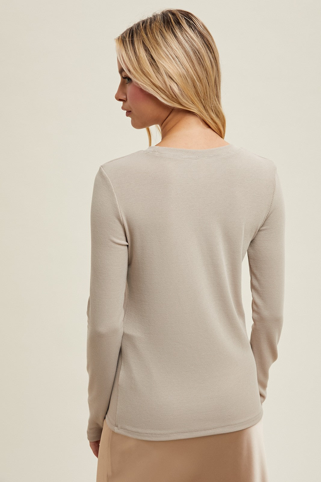 woman wearing a beige long sleeve top with a ribbed texture, viewed from the back