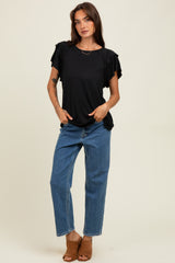 woman wearing a black short sleeve top with ruffle details and blue high-waisted jeans, standing in a neutral background