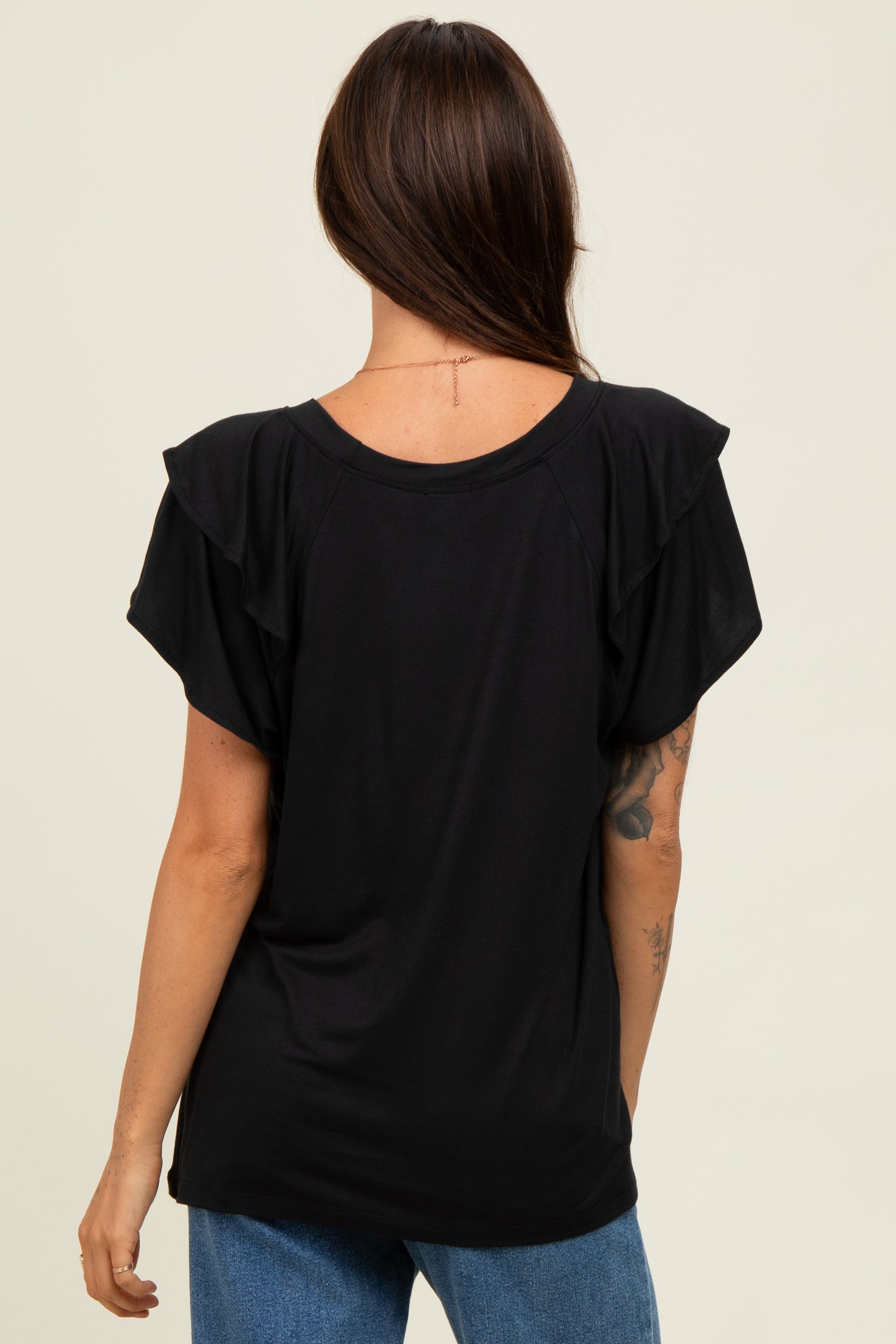 woman wearing a black short sleeve top with ruffle detail and a relaxed fit, viewed from the back