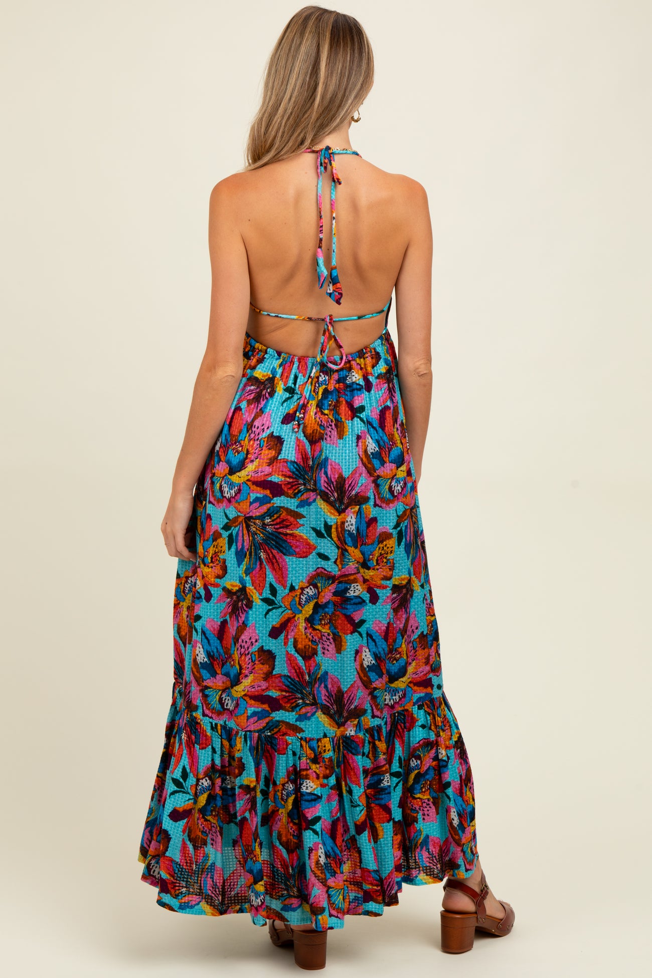 woman wearing a colorful floral maternity maxi dress with a halter neck and ruffled hem, featuring a tie-back detail