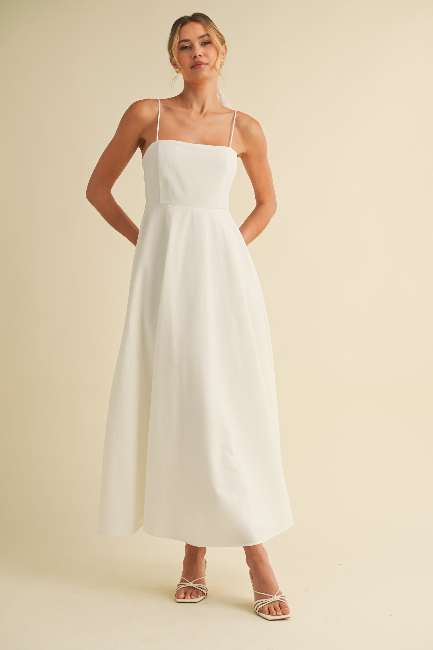 woman wearing a white spaghetti strap maxi dress with a square neckline and a flowy skirt