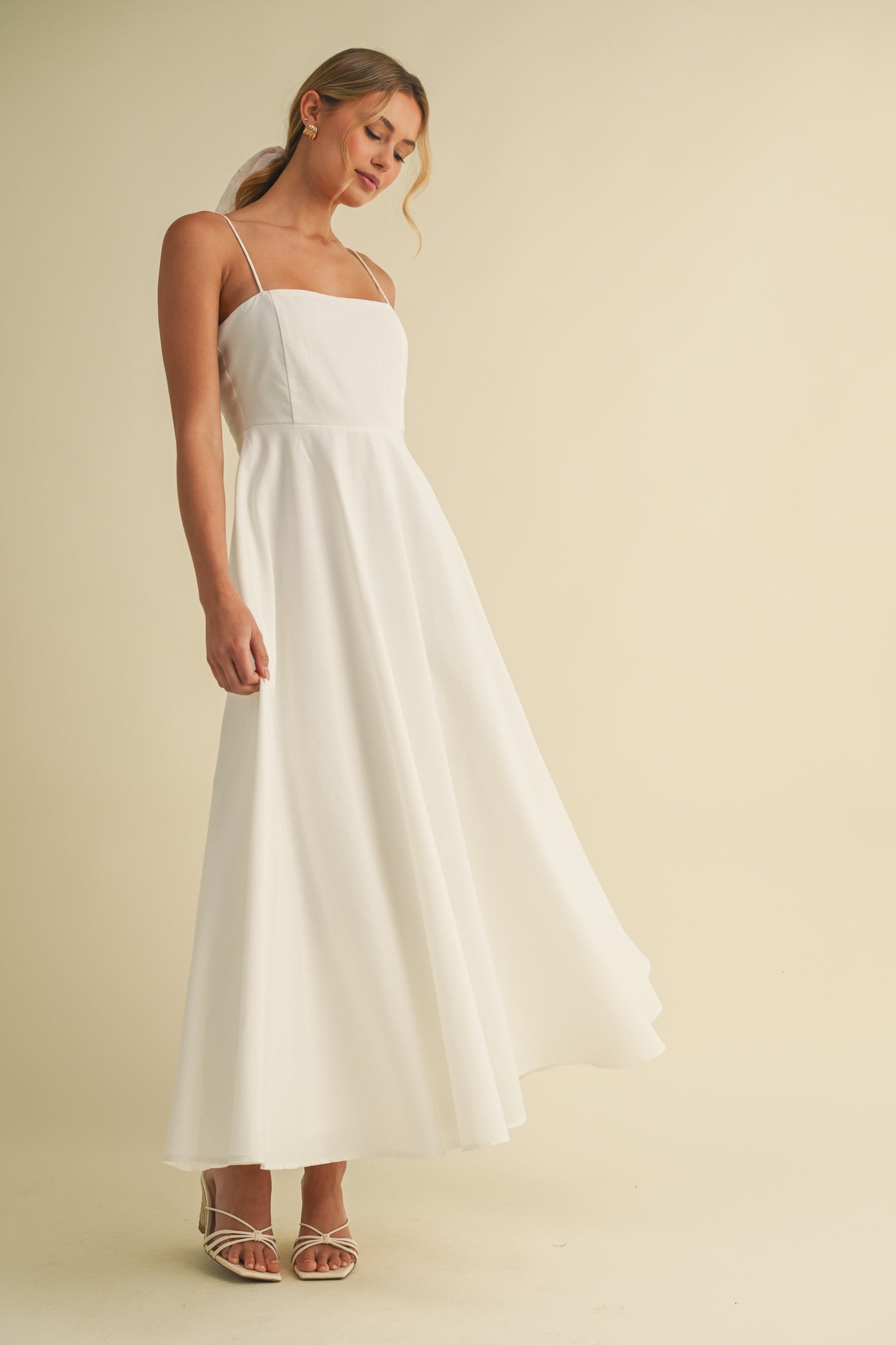 woman wearing a white spaghetti strap maxi dress with a flowing skirt and strappy sandals