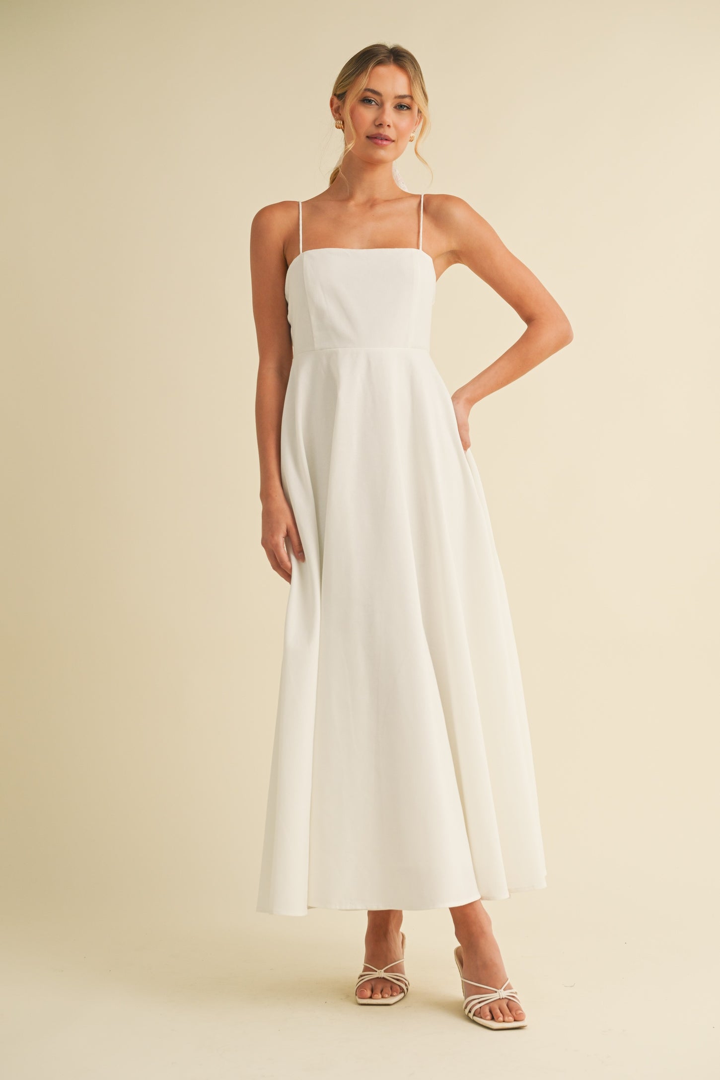 woman wearing a white spaghetti strap maxi dress with a square neckline and pocket details