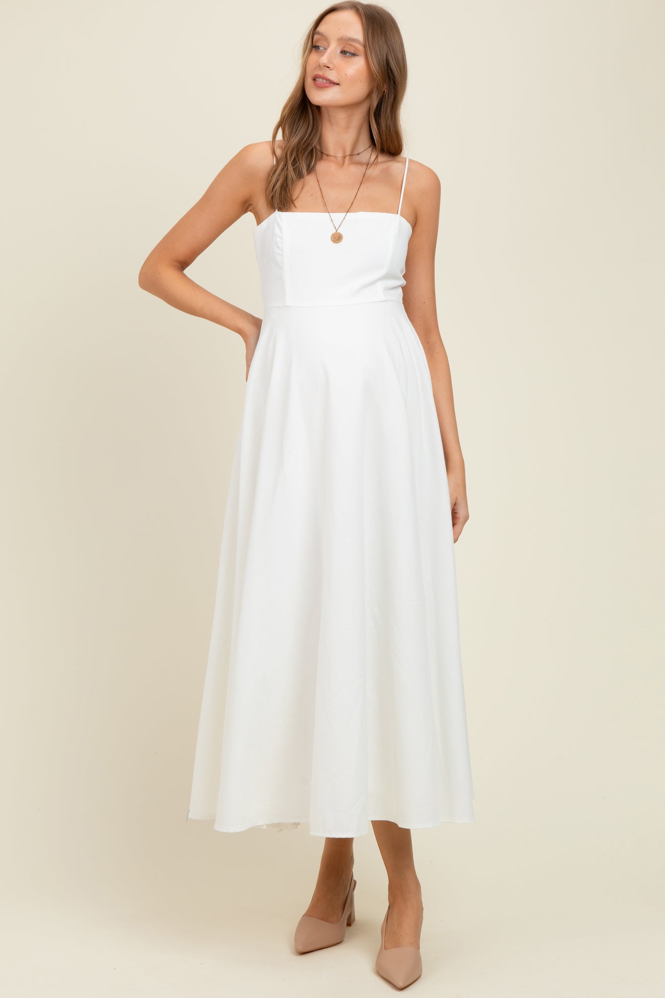 woman wearing a white maternity dress with a square neckline and flowy skirt, showcasing her baby bump