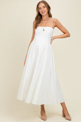woman wearing a white maternity maxi dress with spaghetti straps and a relaxed fit, smiling and posing against a neutral background