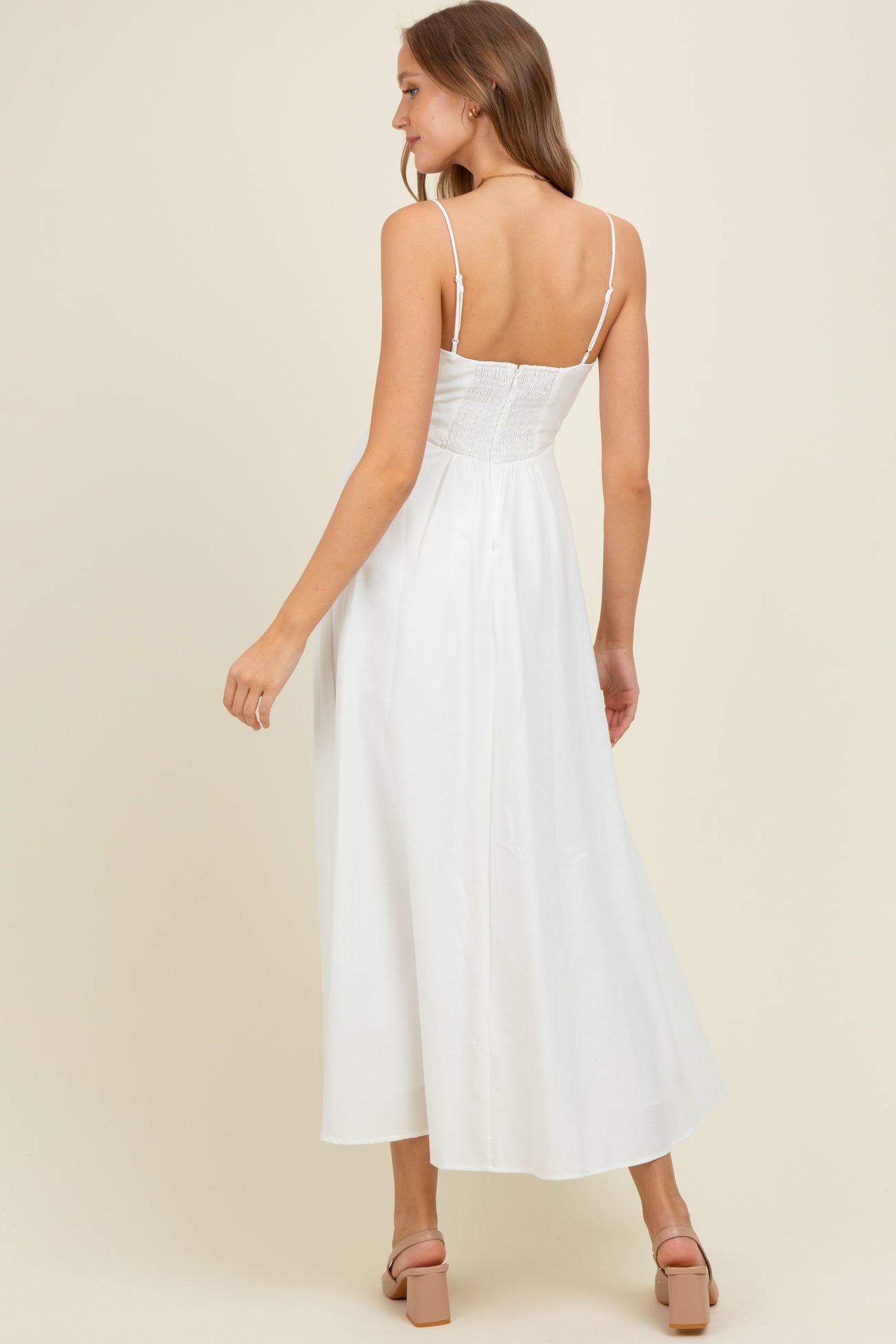 woman wearing a white maternity maxi dress with a smocked bodice and spaghetti straps, showing her back