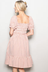 woman wearing a pink and white gingham short sleeve dress with a ruffled hem and smocked back