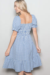woman wearing a blue and white gingham smocked sundress with puff sleeves and a ruffled hem