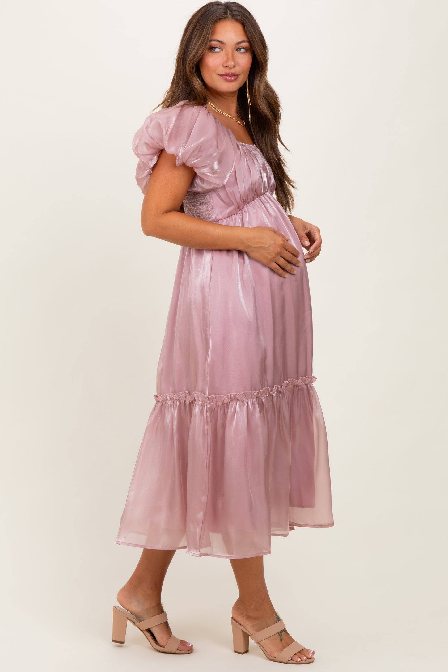 woman wearing a light mauve puff sleeve maternity dress with a ruffled hem and baby bump visible