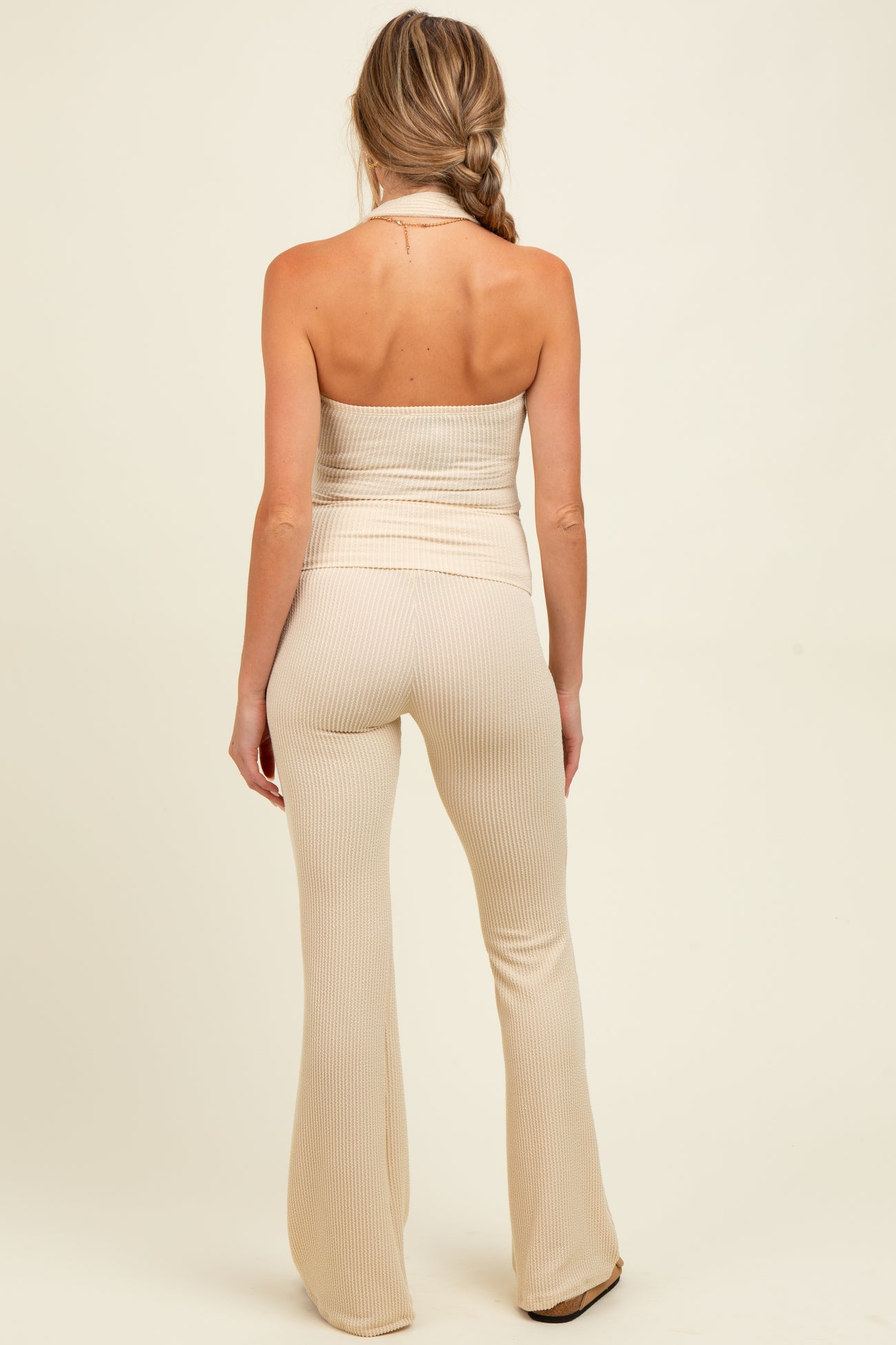 woman wearing a beige maternity ribbed halter top and matching flared pants, showing a smooth back view