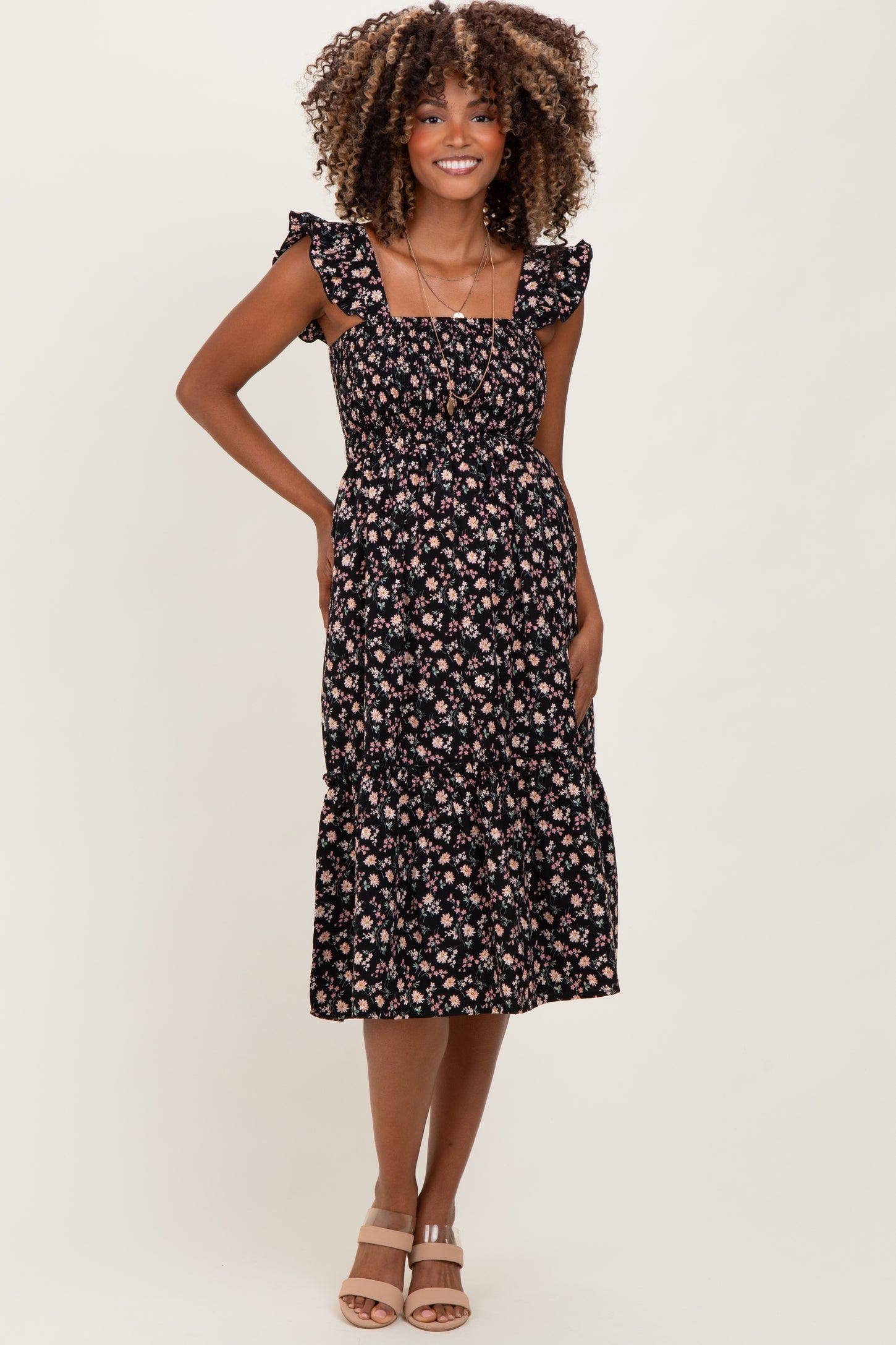 woman wearing a black floral print maternity dress with ruffle straps and a tiered skirt, showcasing her baby bump
