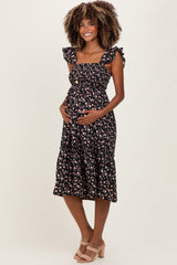 woman wearing a black floral maternity dress with ruffled straps and a baby bump, standing and smiling