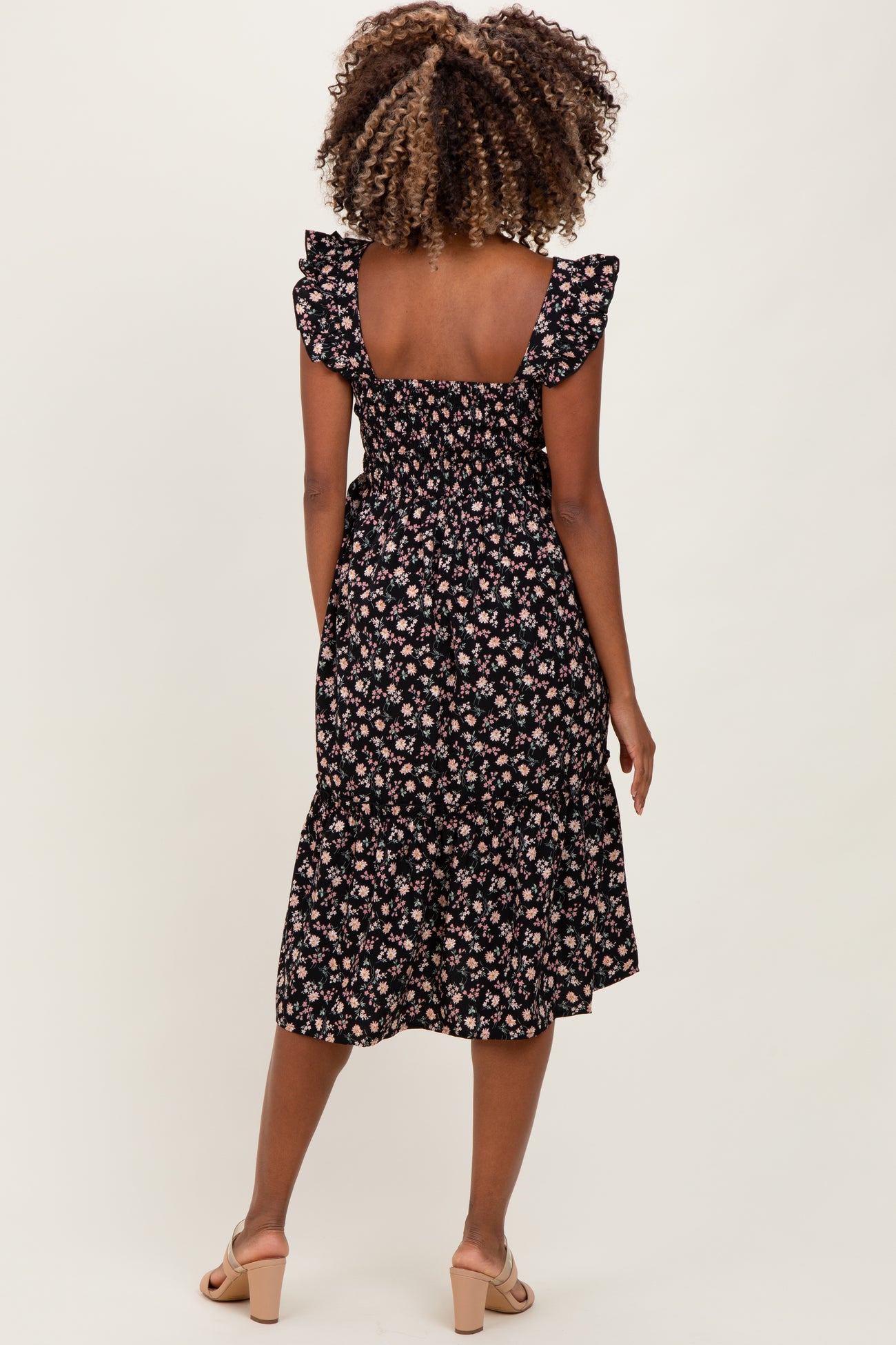 woman wearing a black floral print maternity dress with ruffled sleeves and a flared hem, showing her baby bump from behind