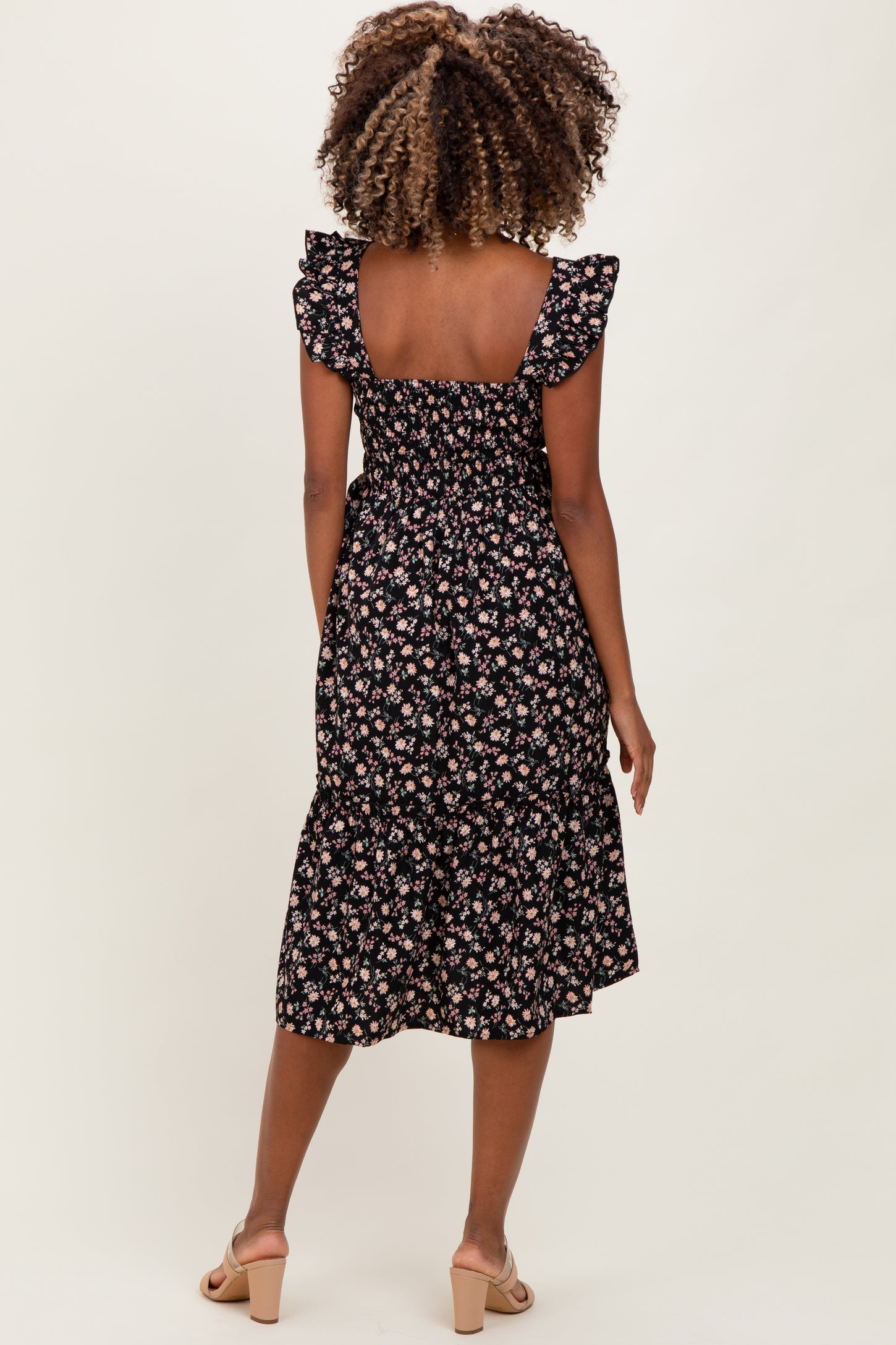 woman wearing a black floral print maternity dress with ruffled sleeves and a flared hem, showing her baby bump from behind