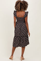 woman wearing a black floral print maternity dress with ruffled sleeves and a flared hem, showing her baby bump from behind