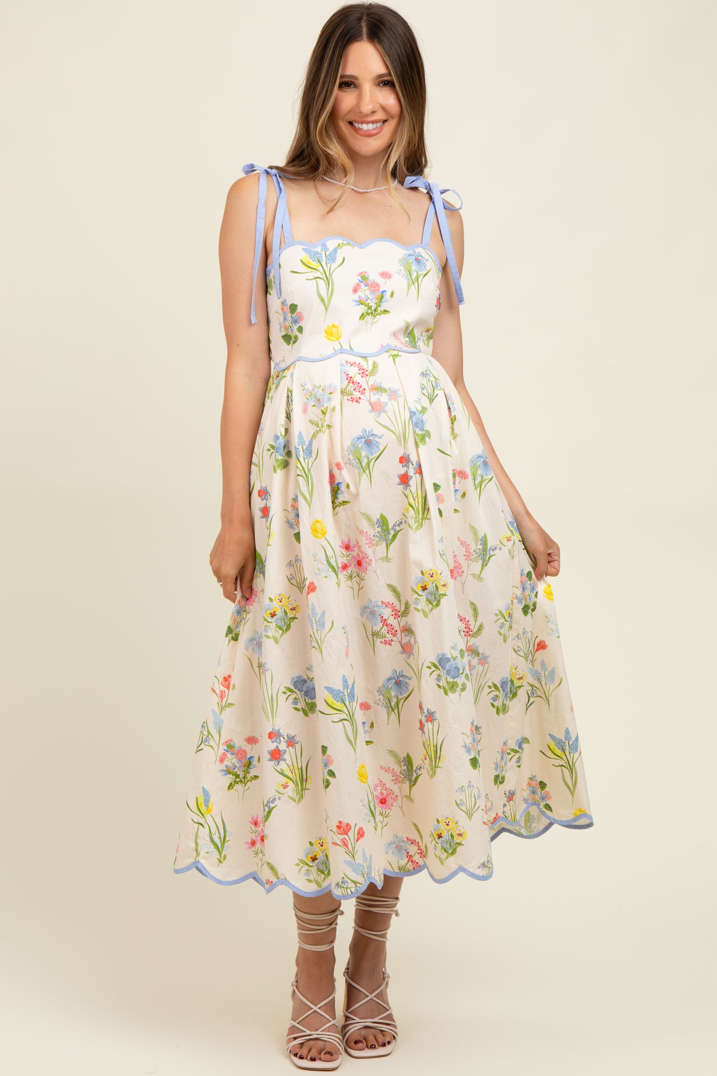 woman wearing a floral maternity dress with spaghetti straps and a scalloped hem, styled with strappy heels