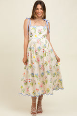 woman wearing a floral maternity dress with spaghetti straps and a scalloped hem, styled with strappy heels