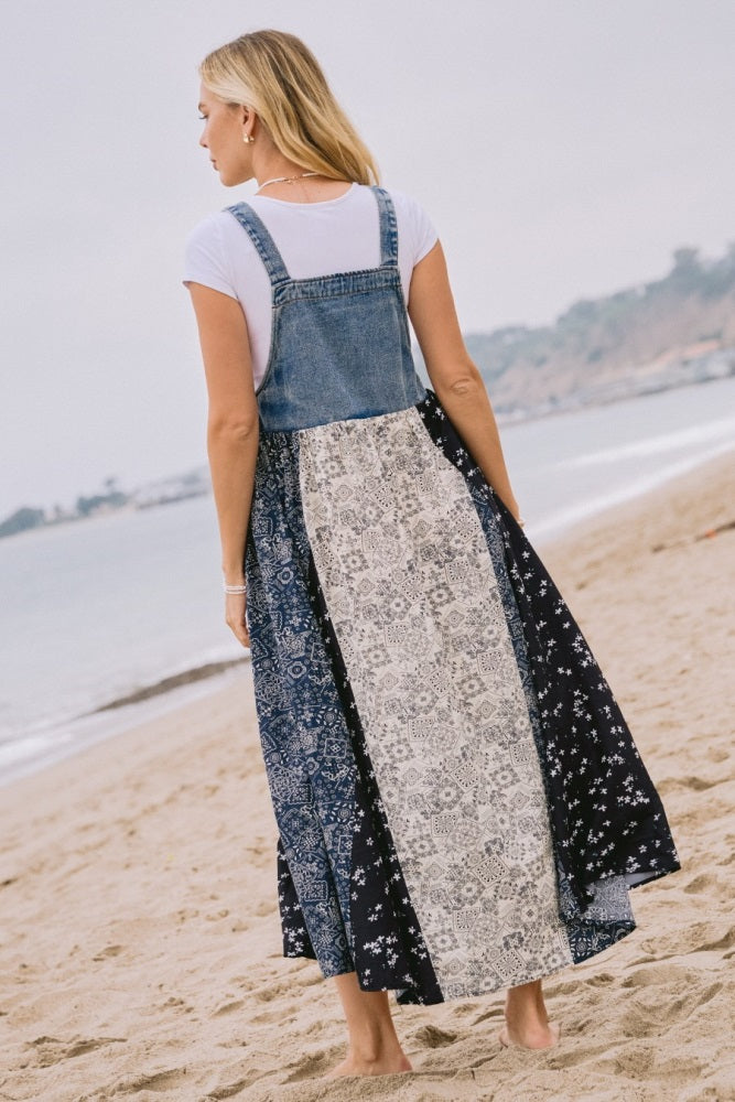 woman wearing a denim and patterned maxi dress over a white t-shirt, standing on the beach with a view of the ocean