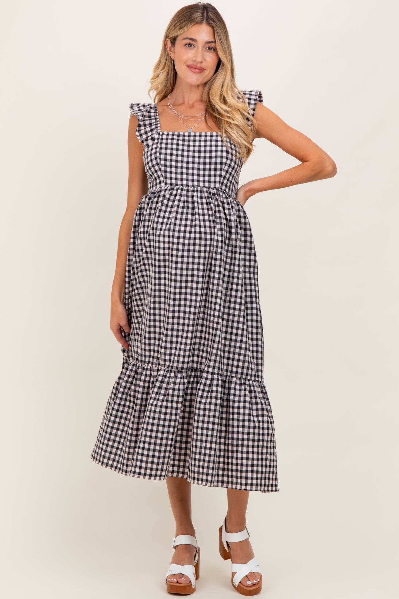 woman wearing a black and white gingham maternity dress with ruffled sleeves and a tiered hem, showing her baby bump