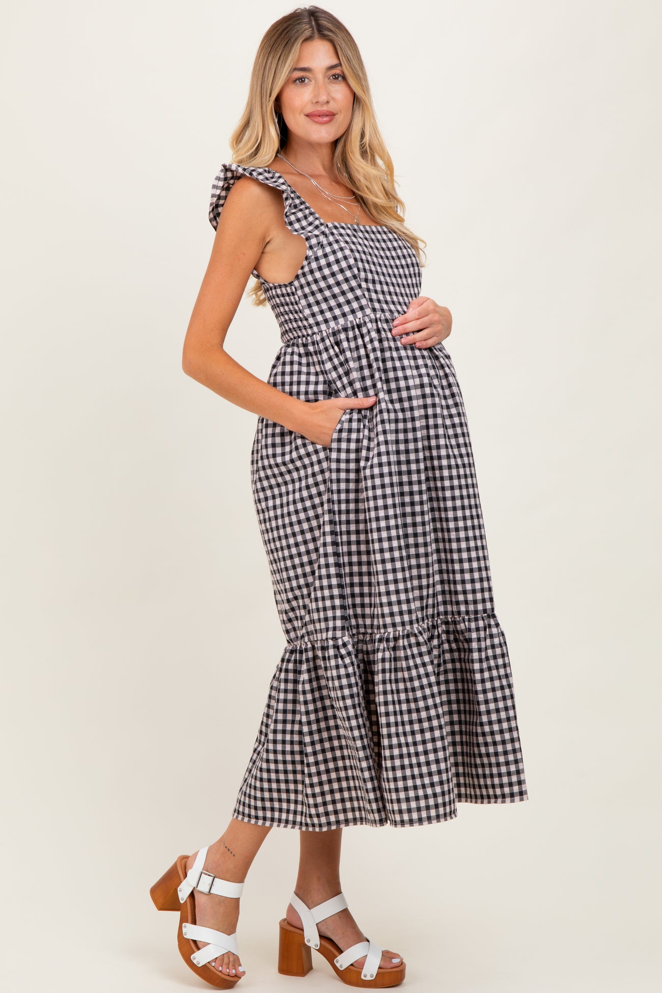 woman wearing a black and white gingham maternity dress with ruffled straps and a tiered skirt, holding her baby bump